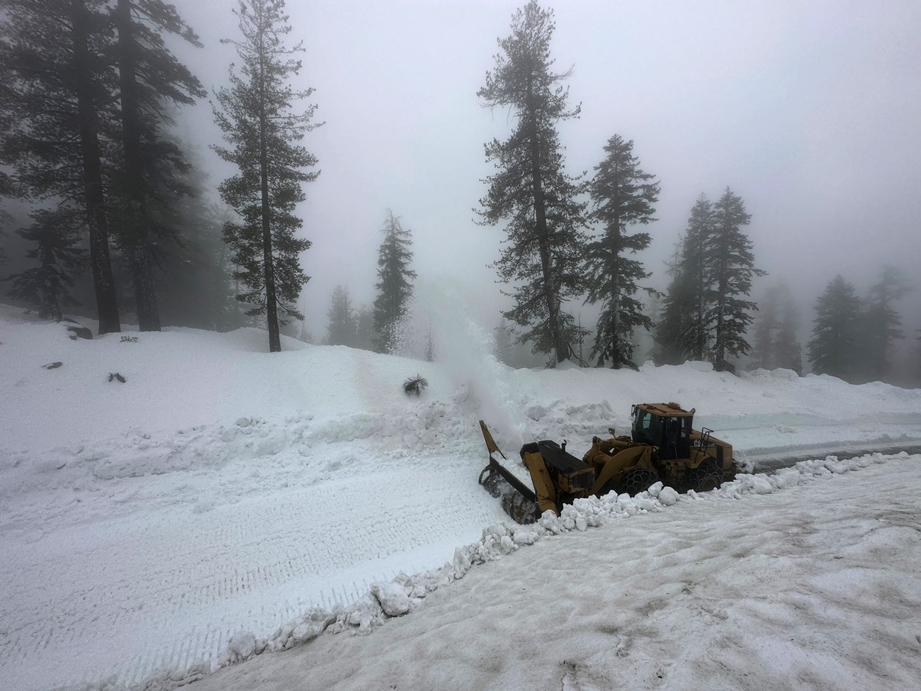 View from above as a blower plows there deep snow on a foggy day