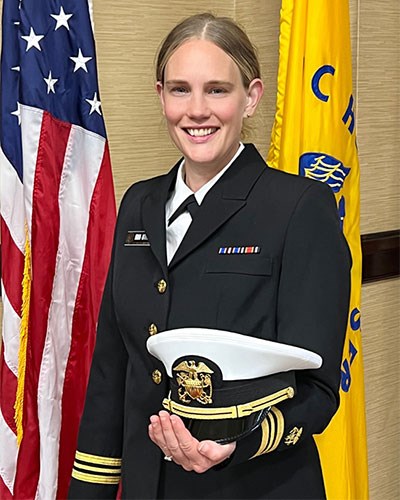 Headshot of Crystal Warren in uniform holding her hat next to an American flag