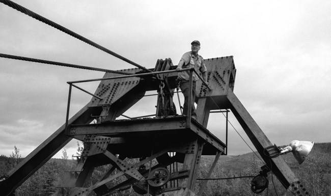 Black and white image of a ranger standing on top of the bucket arm of the Coal Creek Dredge