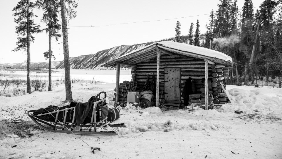 Black and white photograph of a dogsled at a public use cabin on the Yukon River in winter
