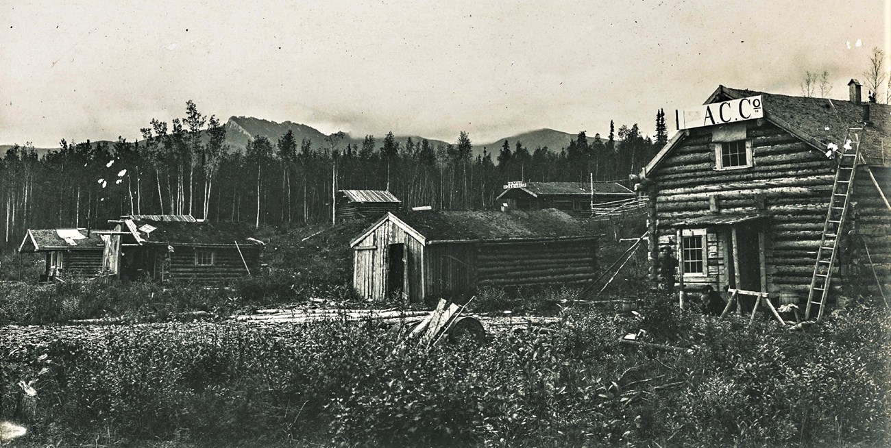 The mining camp of Seventy Mile near where the Seventymile River enters the Yukon River, 1899.  Both the Alaska Commercial Company store and the 70-Mile Roadhouse are sporting signs.