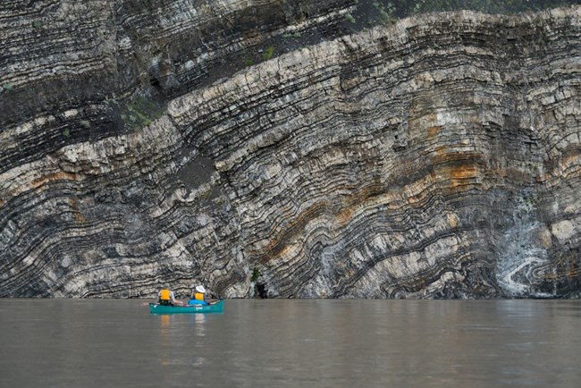 Two people in a boat floating past large layered rock formation