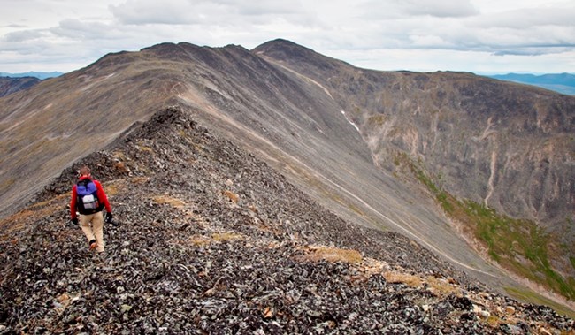 A hiker on a rocky ridgeline with a mountain peak in the distance