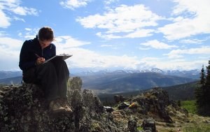 An archaeologist sitting on a boulder sketches a site map.