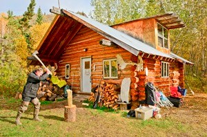 A visitor splits wood in front of the Smith public use cabin