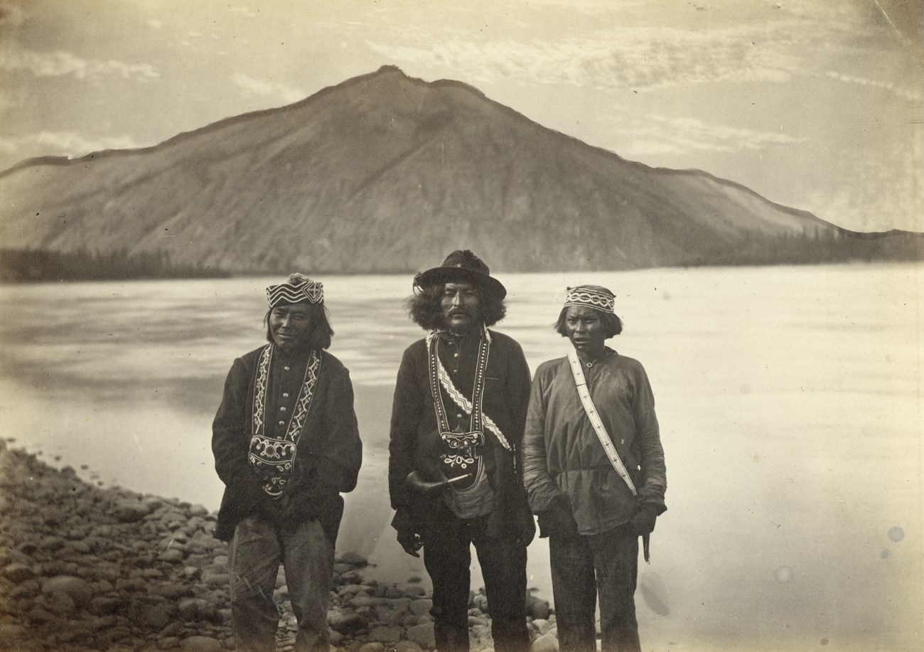 Historic photograph of three Tanana Alaska Natives near what is now Eagle Village on the Yukon River with Eagle Bluff in the background
