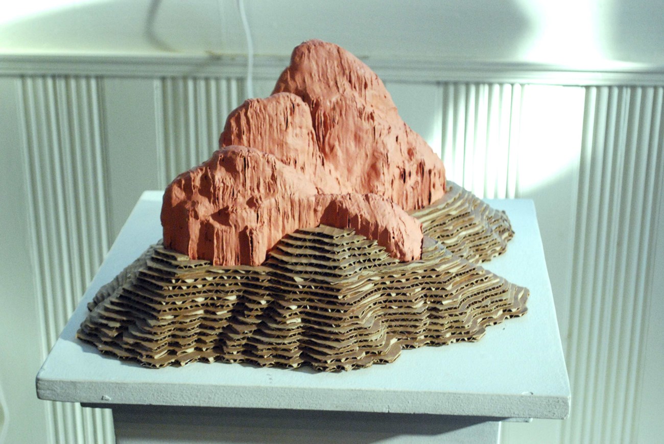 A sculpture on a tabletop resembles the topographic lines of a red mountain.