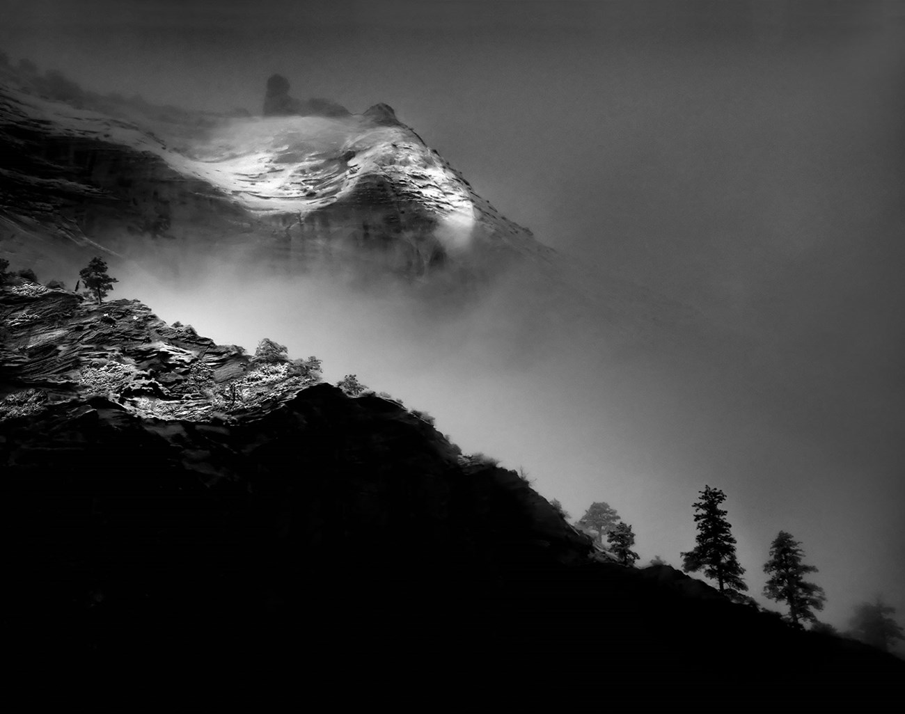 Black and white photo of snow covered canyon walls mostly obscured by fog