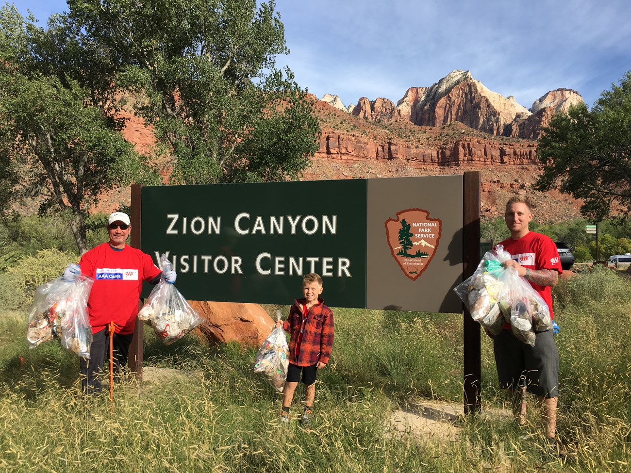 Three people hold bags of garbage they collected near the Zion Canyon Visitor Center