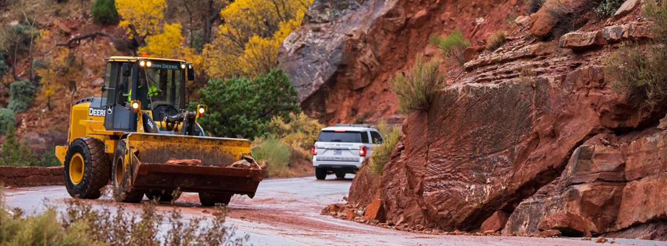 A bulldozer moves a large sandstone boulder from the roadway.