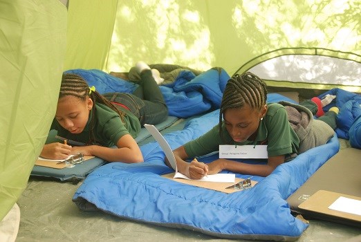 Two students writing in a journal while laying in a tent