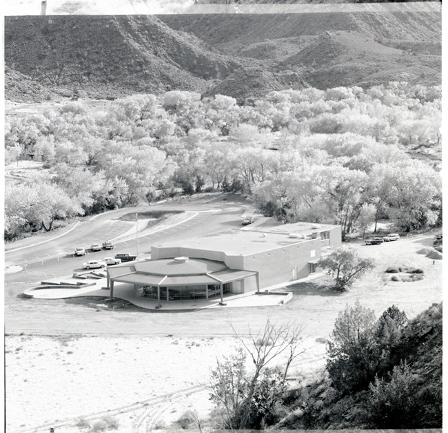 A building stands next to a parking lot with trees in the background.