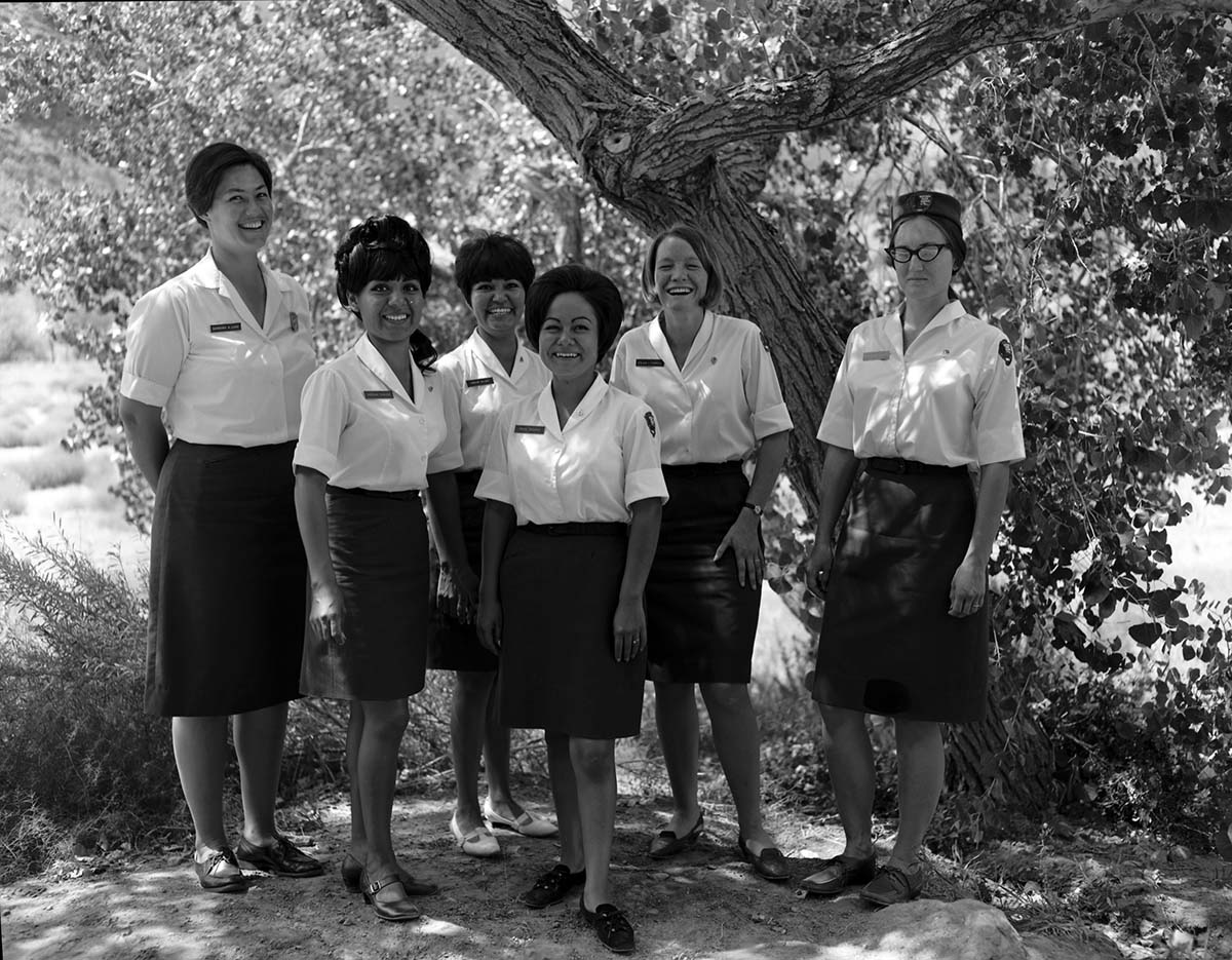 Six uniformed women, in white shirts and black skirts, standing together, smiling at the photographer