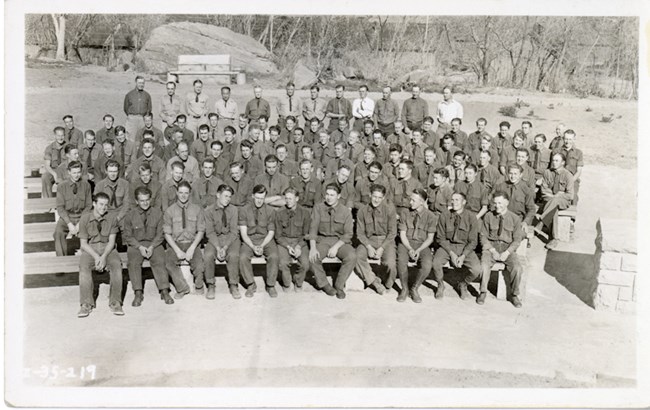 5 ZION 11992: CCC enrollees were divided into companies of about 200 young men. This group photo shows the men of Camp NP-2, along with their overhead personnel. They are seated in the lecture circle, which was completed by the CCC in 1935.