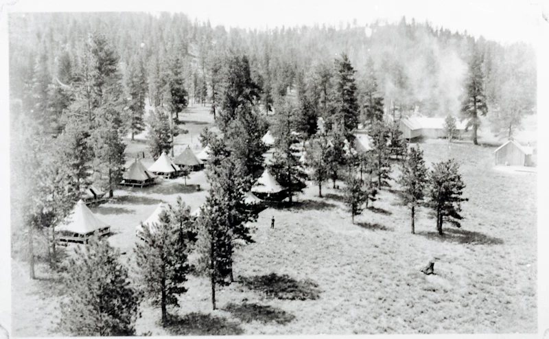 Bryce Canyon CCC Camp Black and white photo of white tents and pine trees scattered in a field with hills behind.