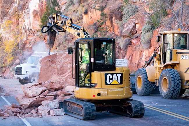 Excavator with pneumatic hammer next to large piece of fallen Navajo Sandstone on a road in Zion National Park