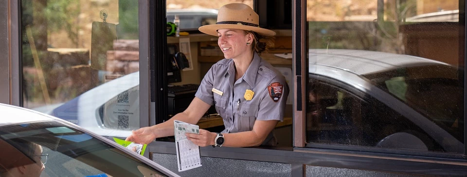 ZionEntranceStations01 A National Park Service Fee Collector smiles as a visitor hands her their entry pass.