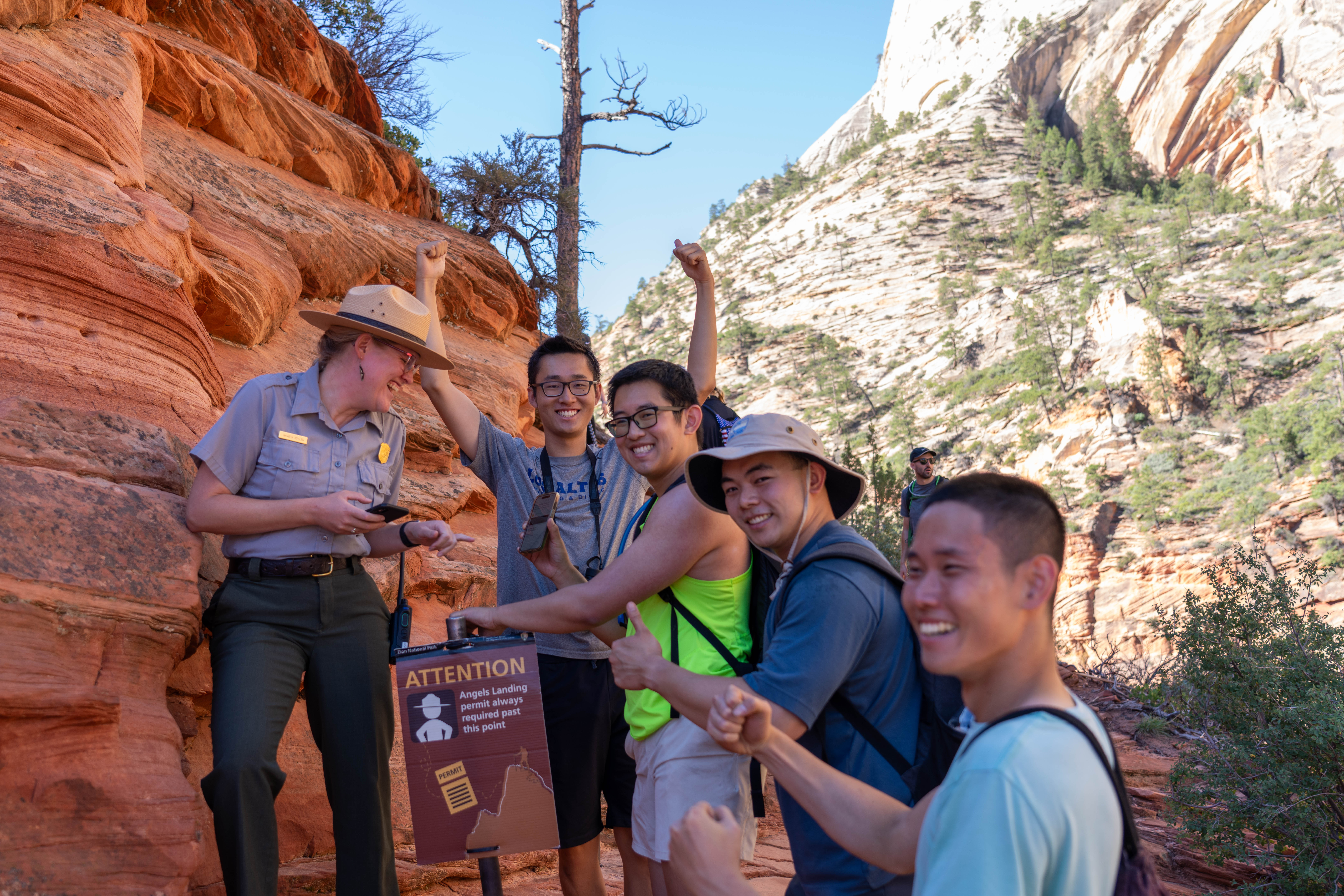 A ranger looking at a permit as vistiors smile at the chain section fo Angels Landing