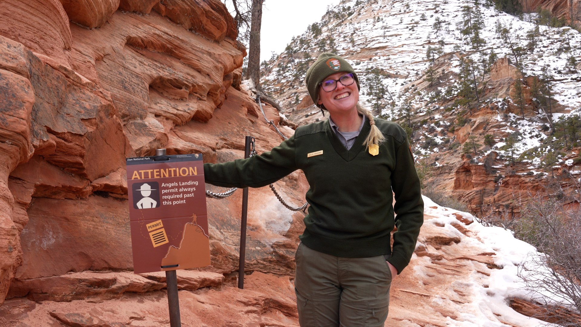 Ranger stands next to a post with a sign about Angels Landing Permits.