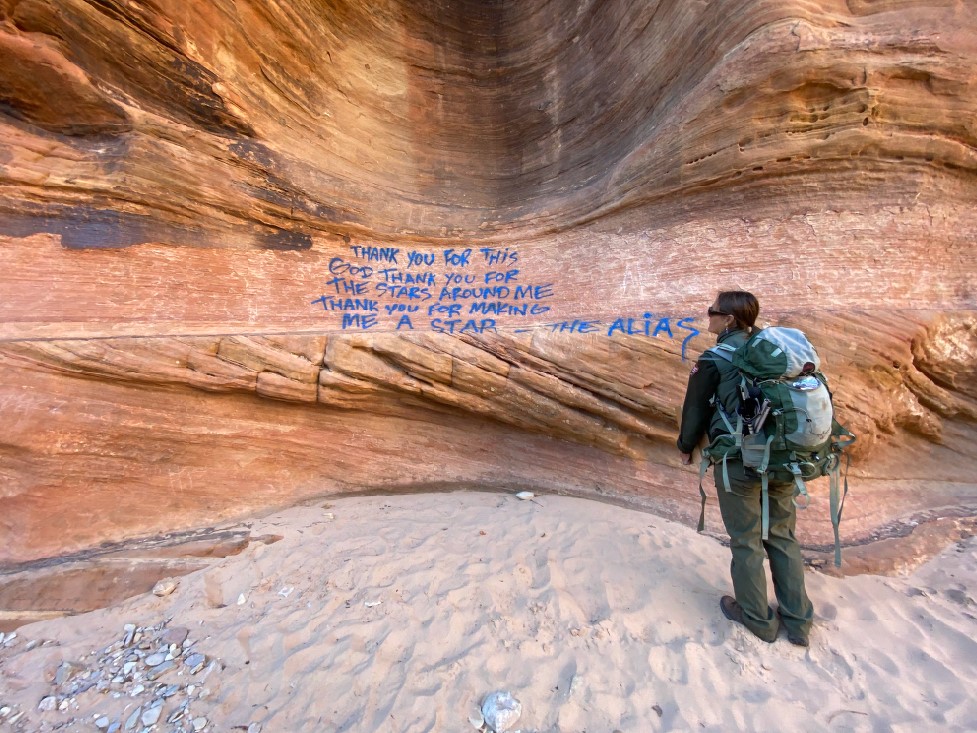 A ranger stand next to a sandstone wall that has blue spray paint graffiti