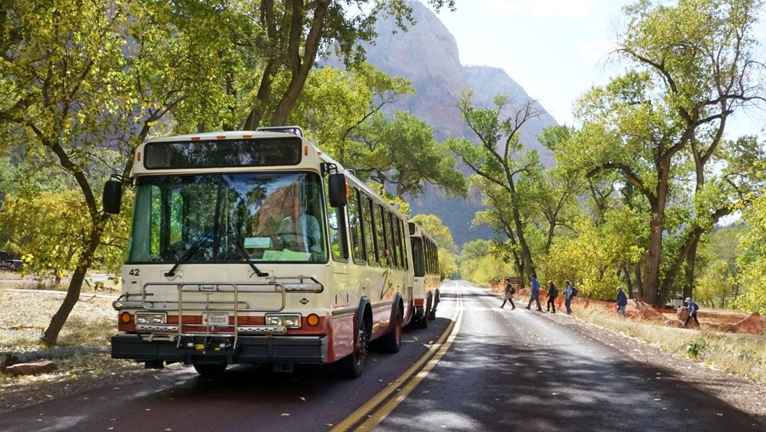 Zion National Park shuttle Front of shuttle bus on road near crosswalk with trees and red rock near the road.