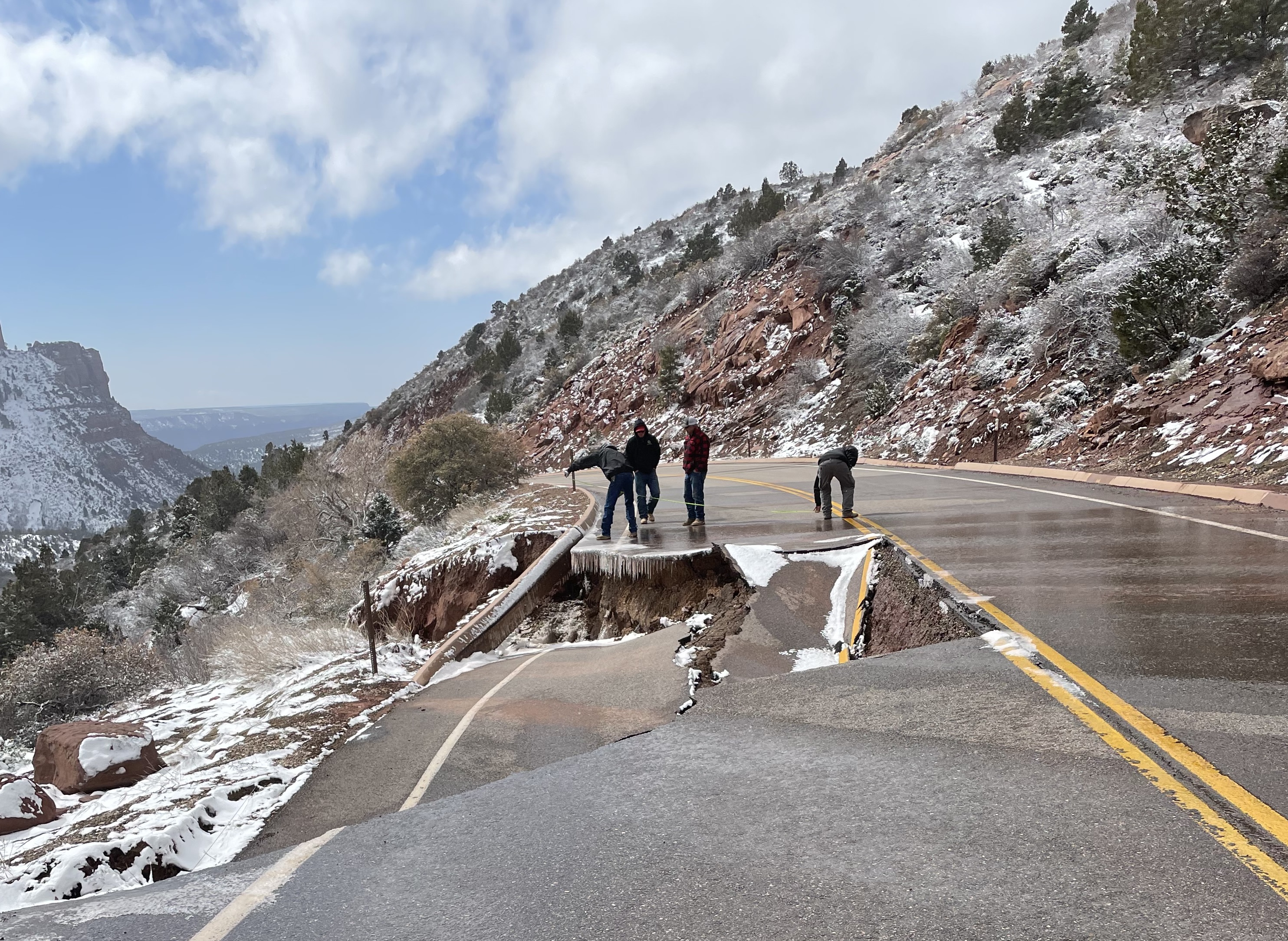 Kolob Canyons Road Zion National park Four people stand near a collapsed section of road that has ice and snow near it.