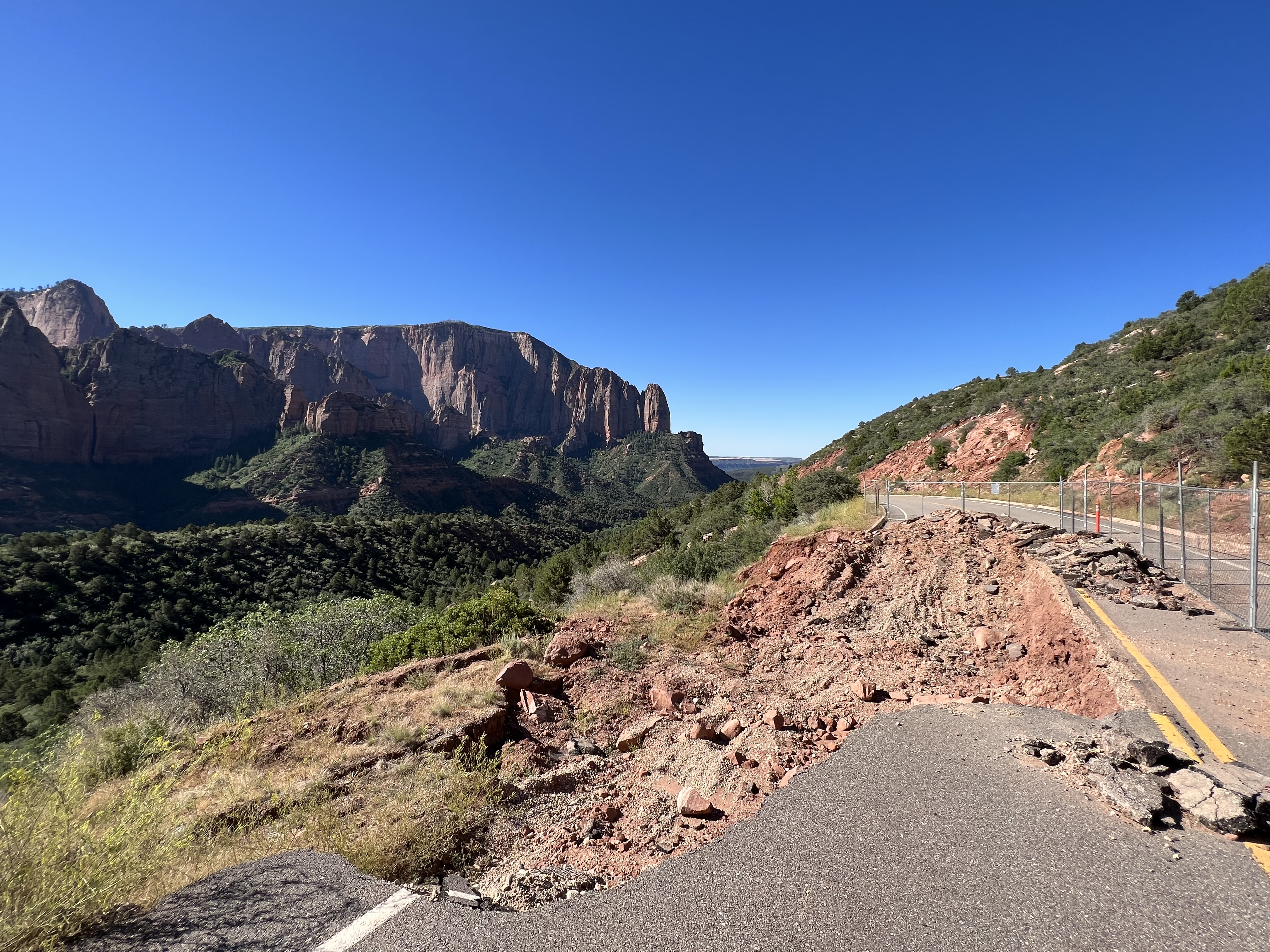 A large hole cutting into a road with greenery and sandstone cliffs in the background