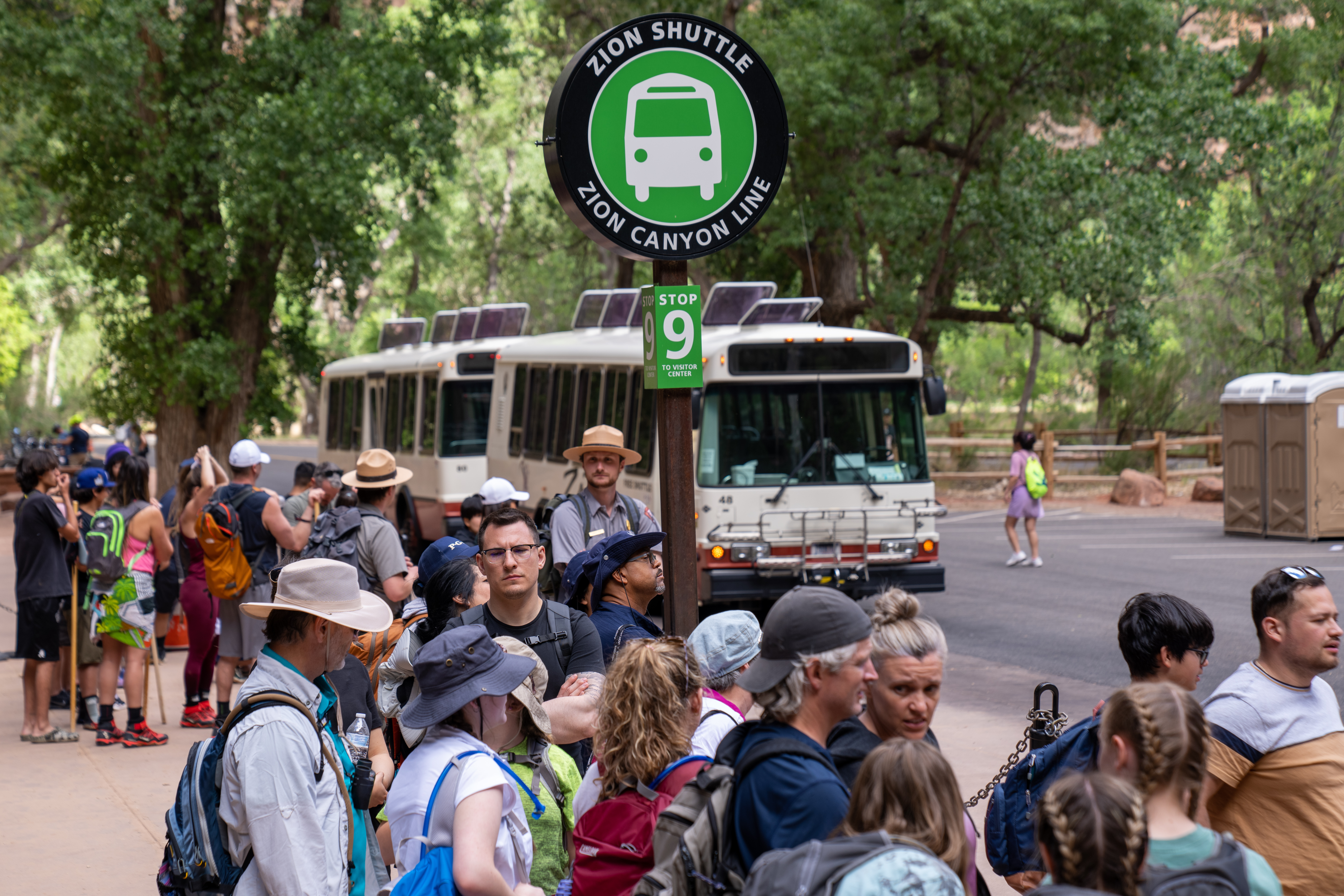 Zion National Park Memorial Day Weekend 2022 Line of visitors waits to board shuttles at Temple of Sinawava in Zion National Park. Two uniformed NPS rangers standby to direct traffic.