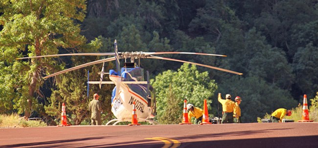 Helicopter sits on ground with several people in yellow shirts near it.