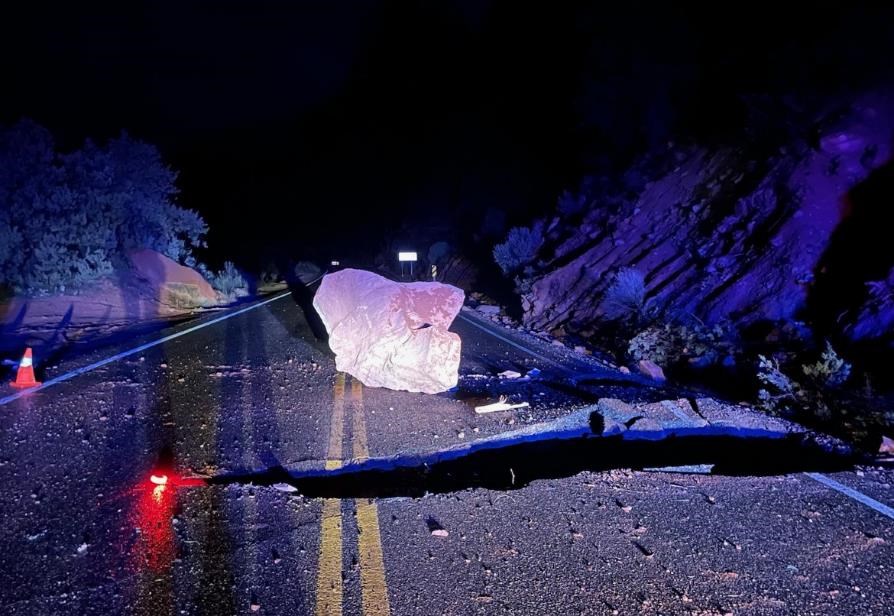 Large rock in road next to a large hole in the road at night Zion National Park. Road flares mark road damage.