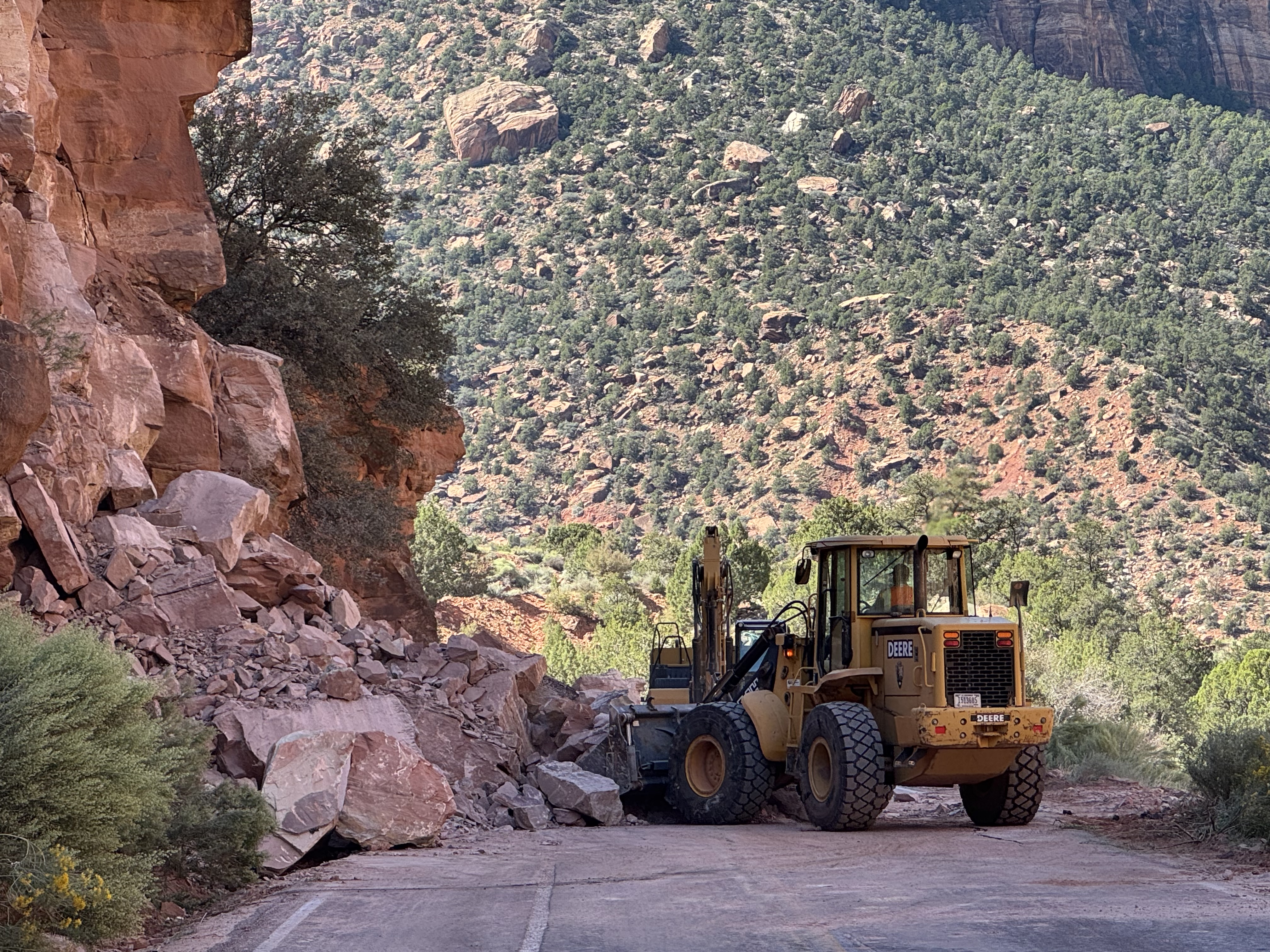 A large yellow construction vehicle pushes rocks and debris off a roadway.