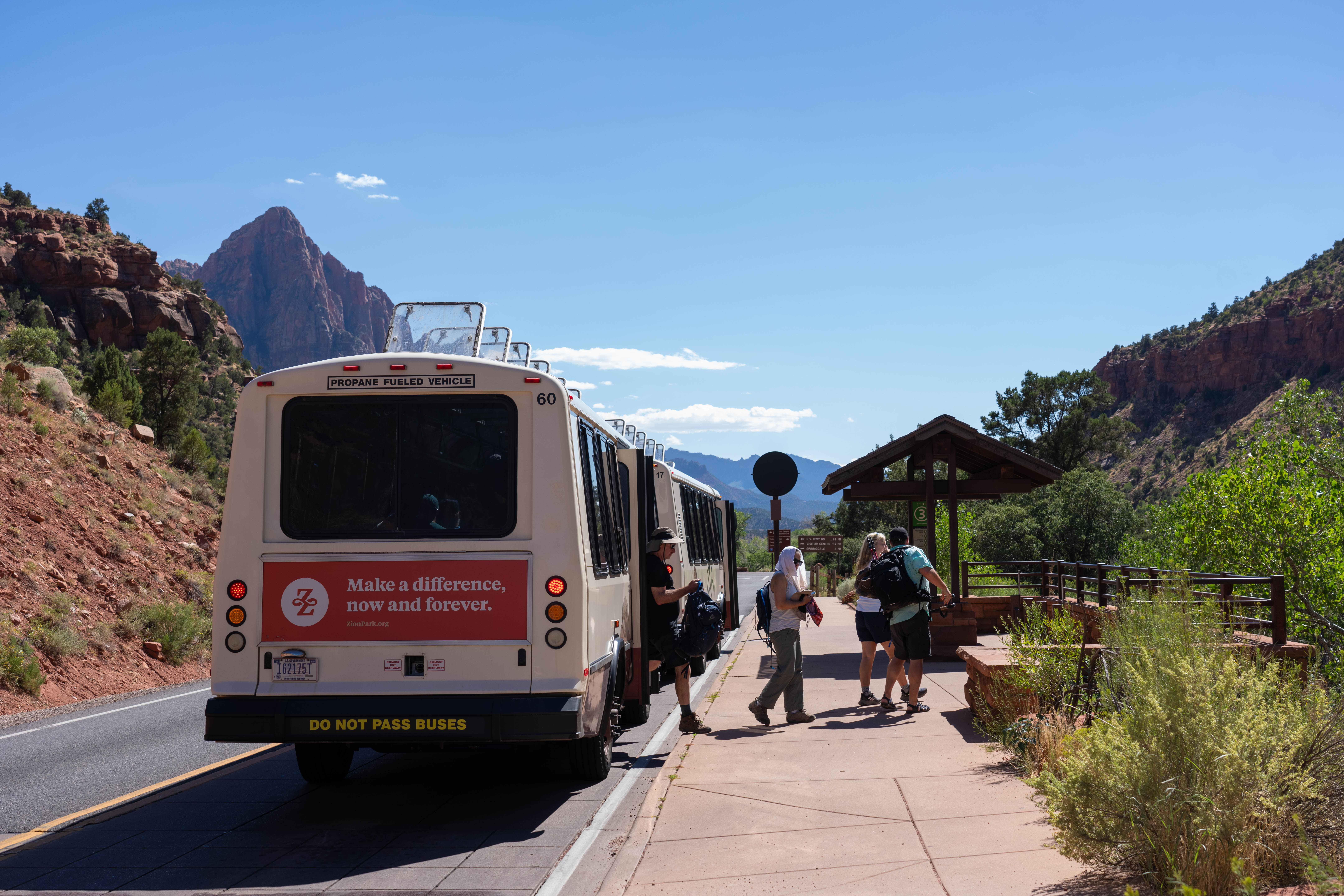Visitors deboarding the Zion shuttle with sandstone cliffs in the background