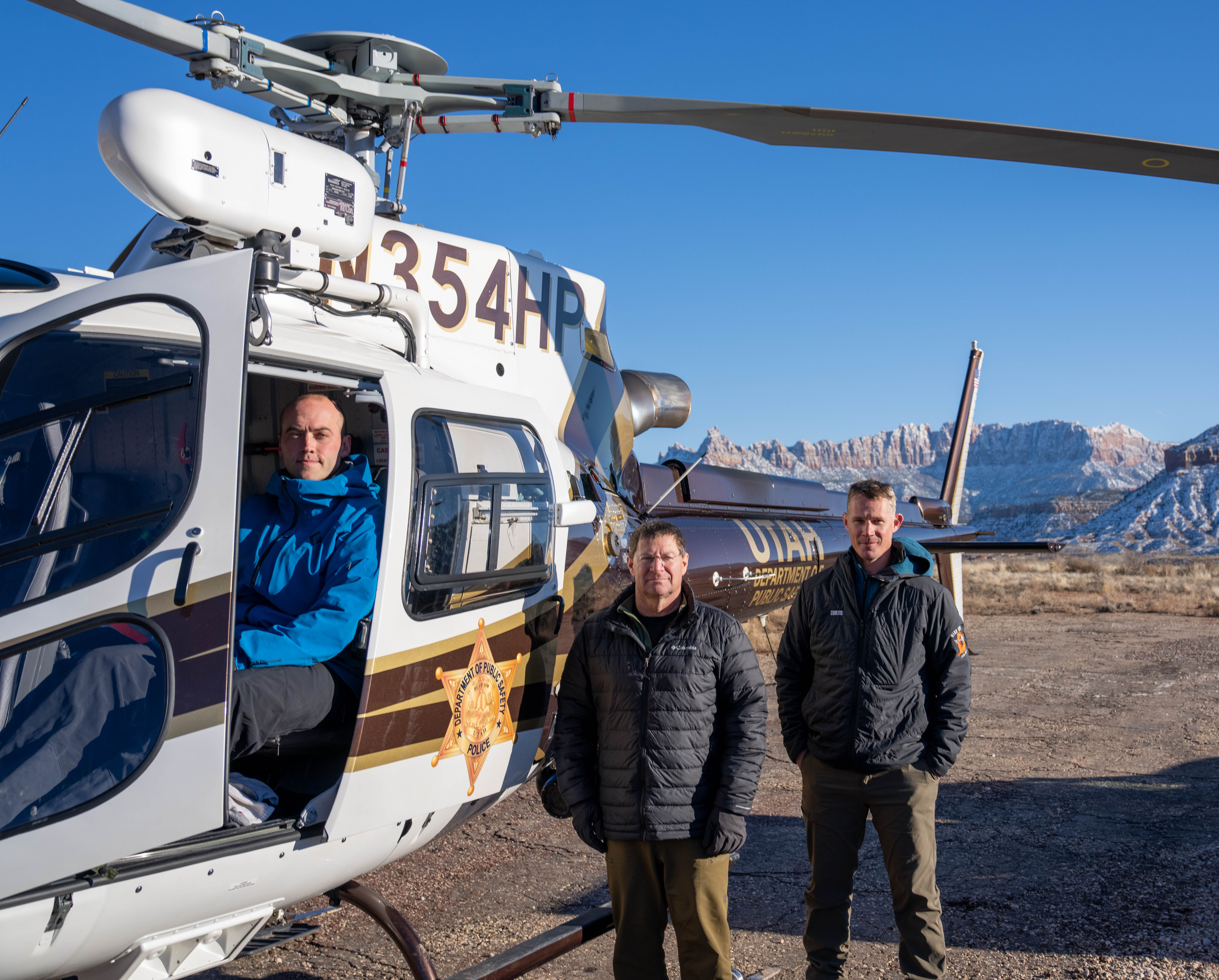 Three people stand in front of a helicopter in Zion National Park