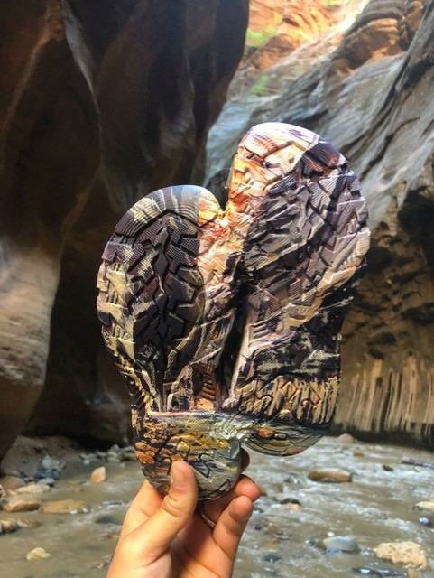 Person holds painted pair of sandals that looks like the Narrows.