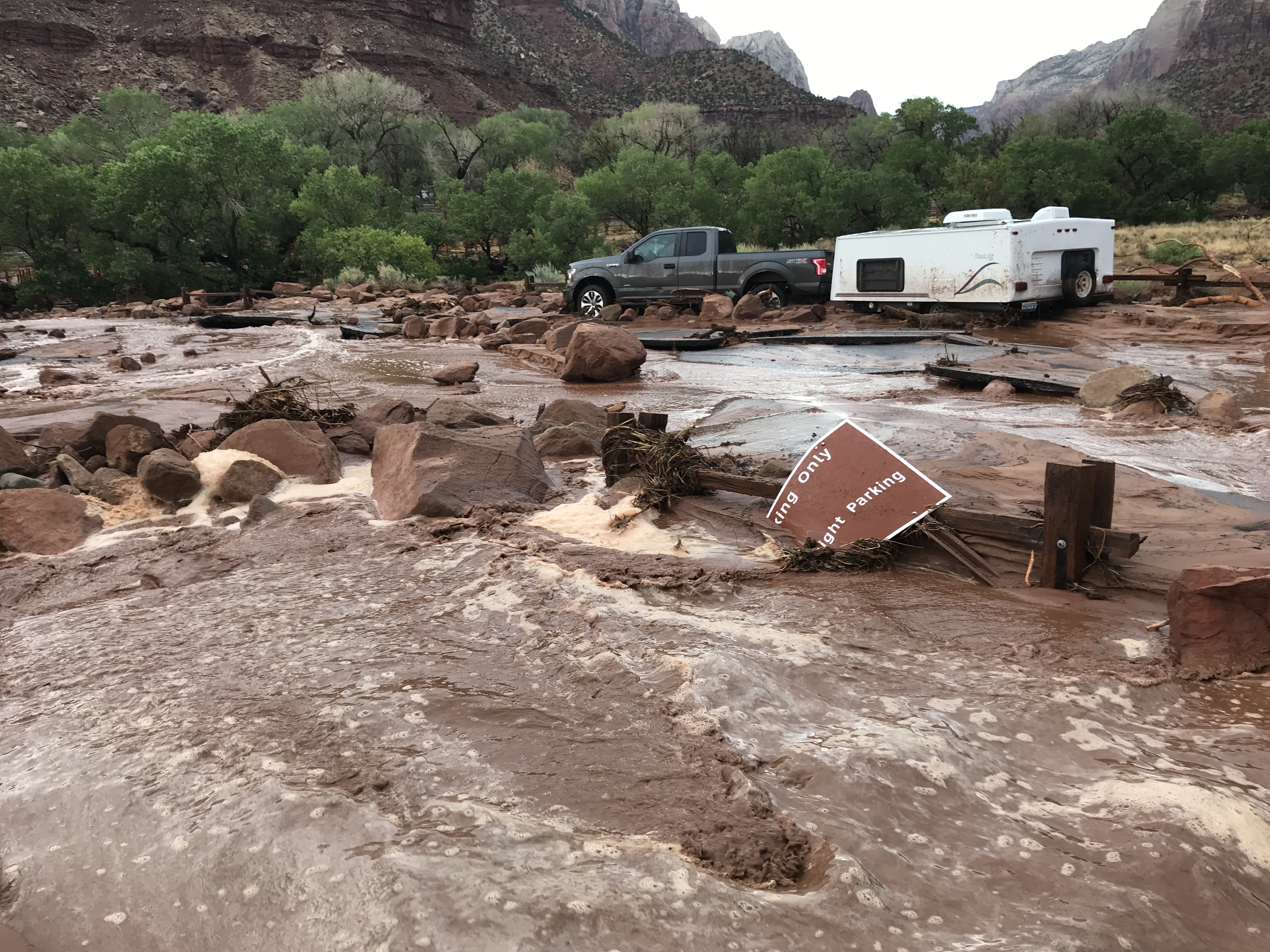 Mud and debris in parking lot, truck with white trailer immersed in debris.