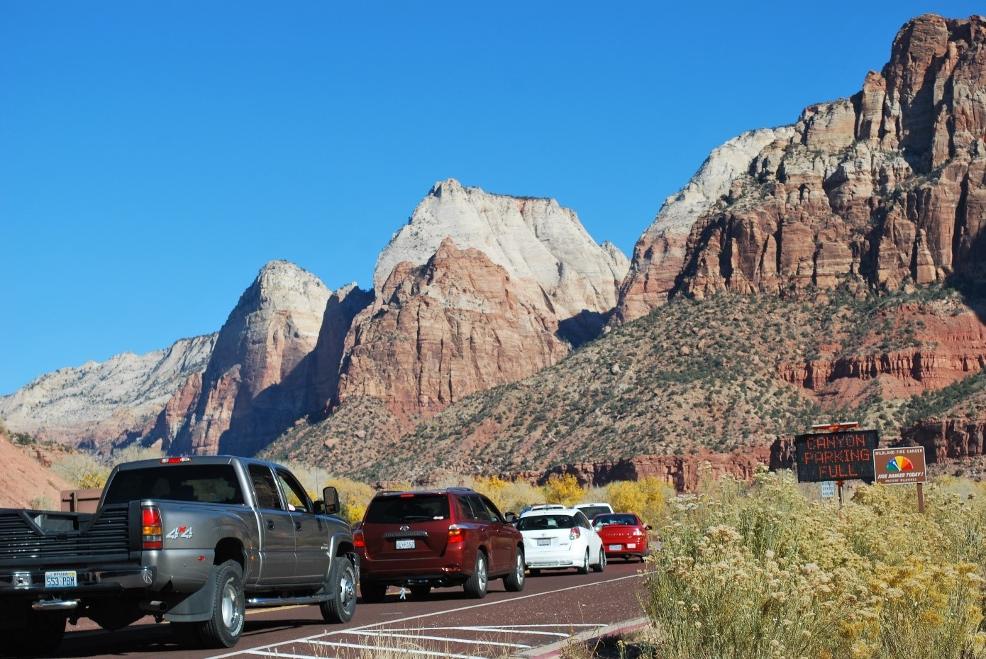 cars waiting in line on the road with sandstone cliffs in the background