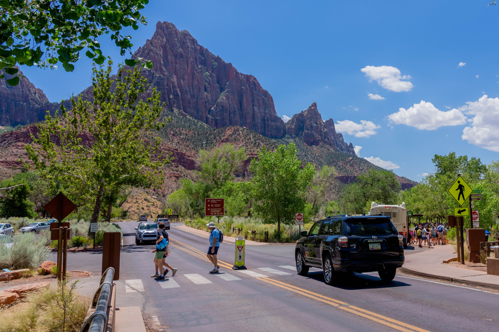 New roadway changes are coming to Zion National Park’s South Entrance Image shows visitors crossing a road. A vehicle is stop for pedestrians.