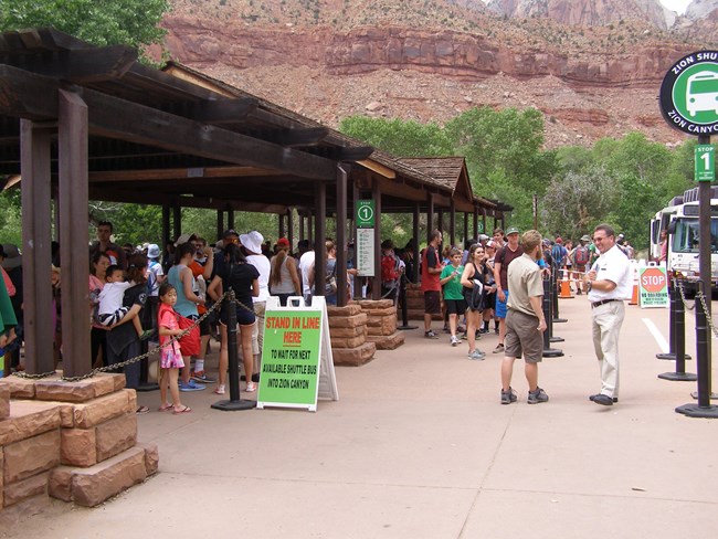 People wait under a wooden shade shelter for the next shuttle