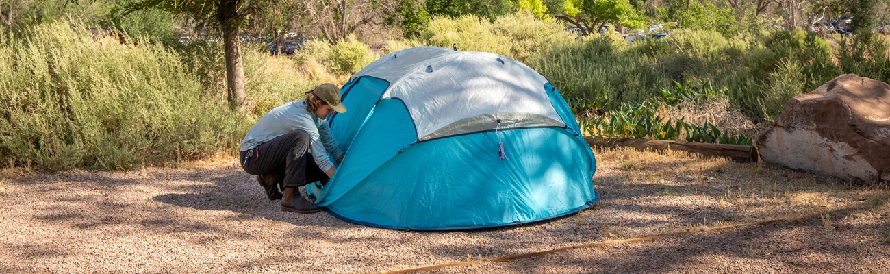 A person sets up a bright blue tent at a campground.