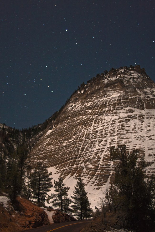 Stars in a twilight sky, over a mesa crossed with snowy lines