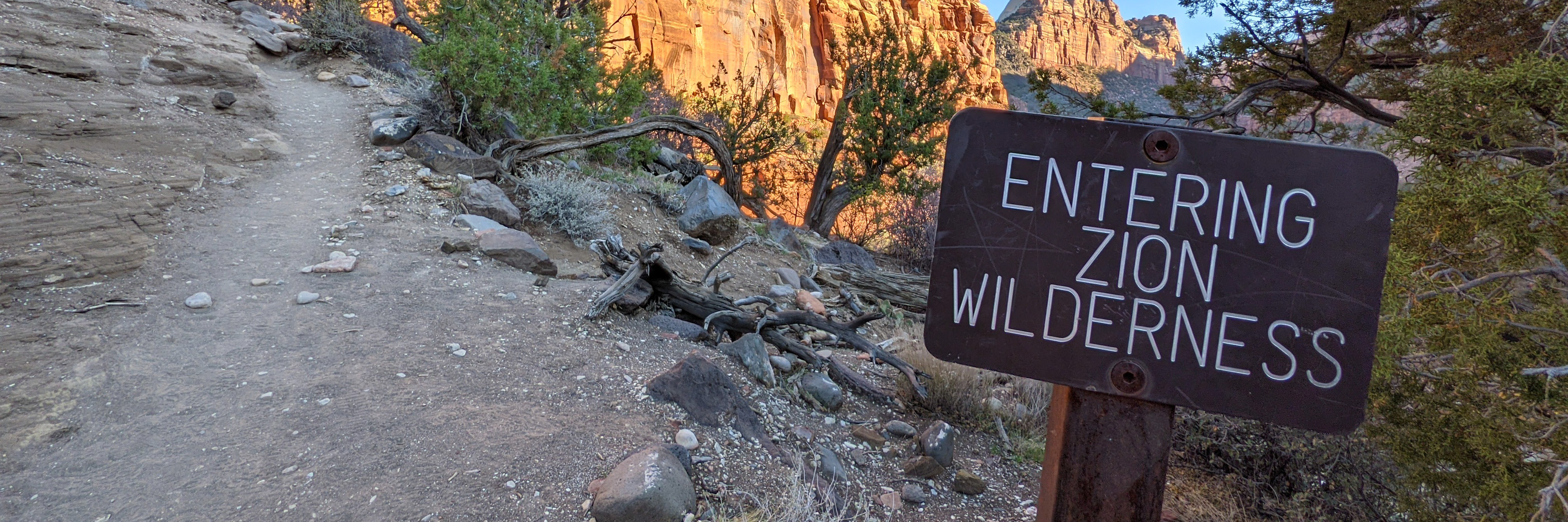A sign along a sandy trail reads "Entering Zion Wilderness."