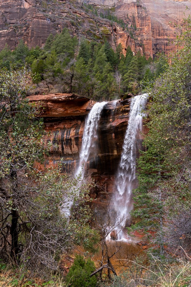 A double waterfall cascades over the edge of a sandstone cliff.