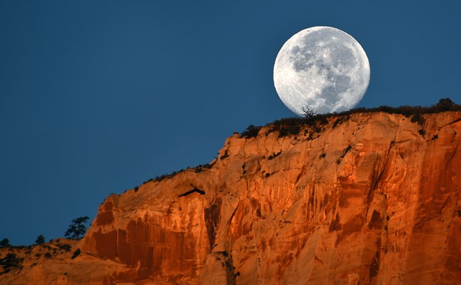 A full moon rising over red cliffs