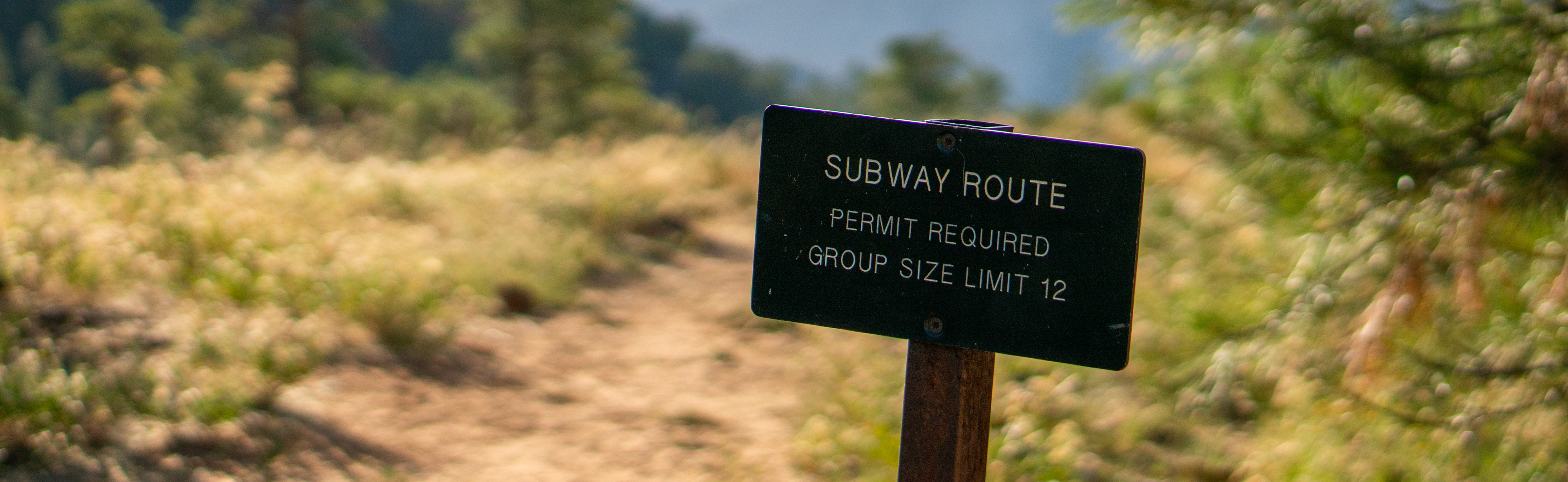 A sign reading "Subway Route, Permit Required, Group Size Limit 12." A grassy trail is seen in the background.