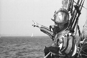 black and white image of a man standing on a ship pointing out across the water