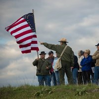 A ranger with visitors on a grass field points past a US flag held by a Civil War reenactor.