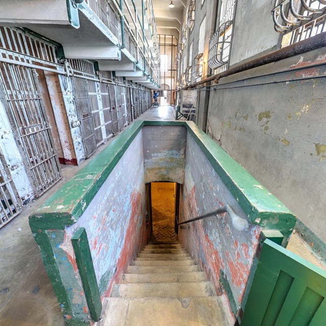 Photograph of corridor of prison cells with stairs leading into basement