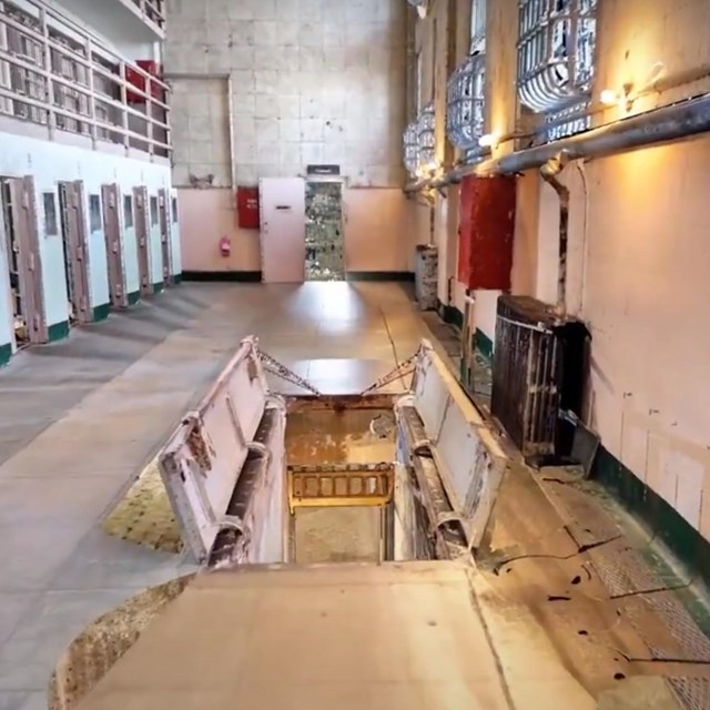 Photograph of prison corridor with open trapdoor leading to basement stairs