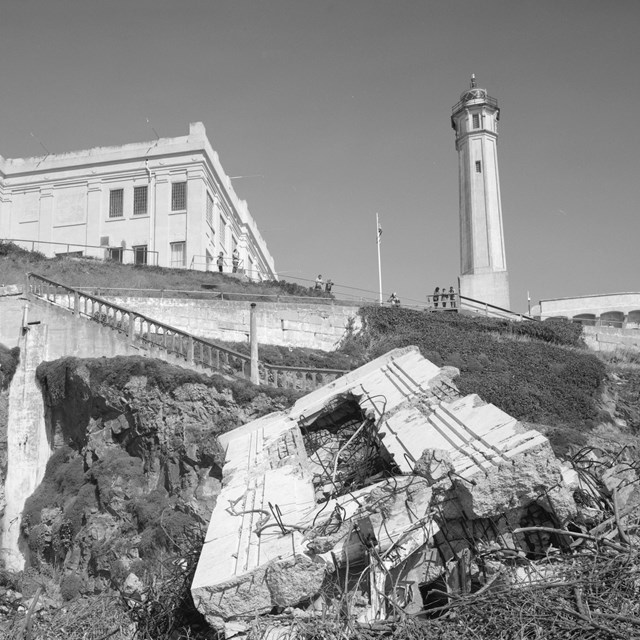 Grayscale photo of prison building on cliff with watchtower and broken concrete
