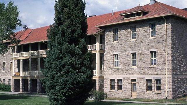 A masonry structure with red metal roof and tree in front